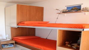Een slaapkamer met een stapelbed, een houten garderobe, een klein bureau met lamp en een plank met een model schip en een foto.