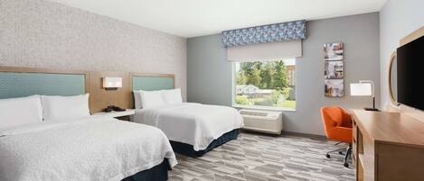 A hotel room with two beds, a desk, an orange chair, a large window, and a flat-screen TV.