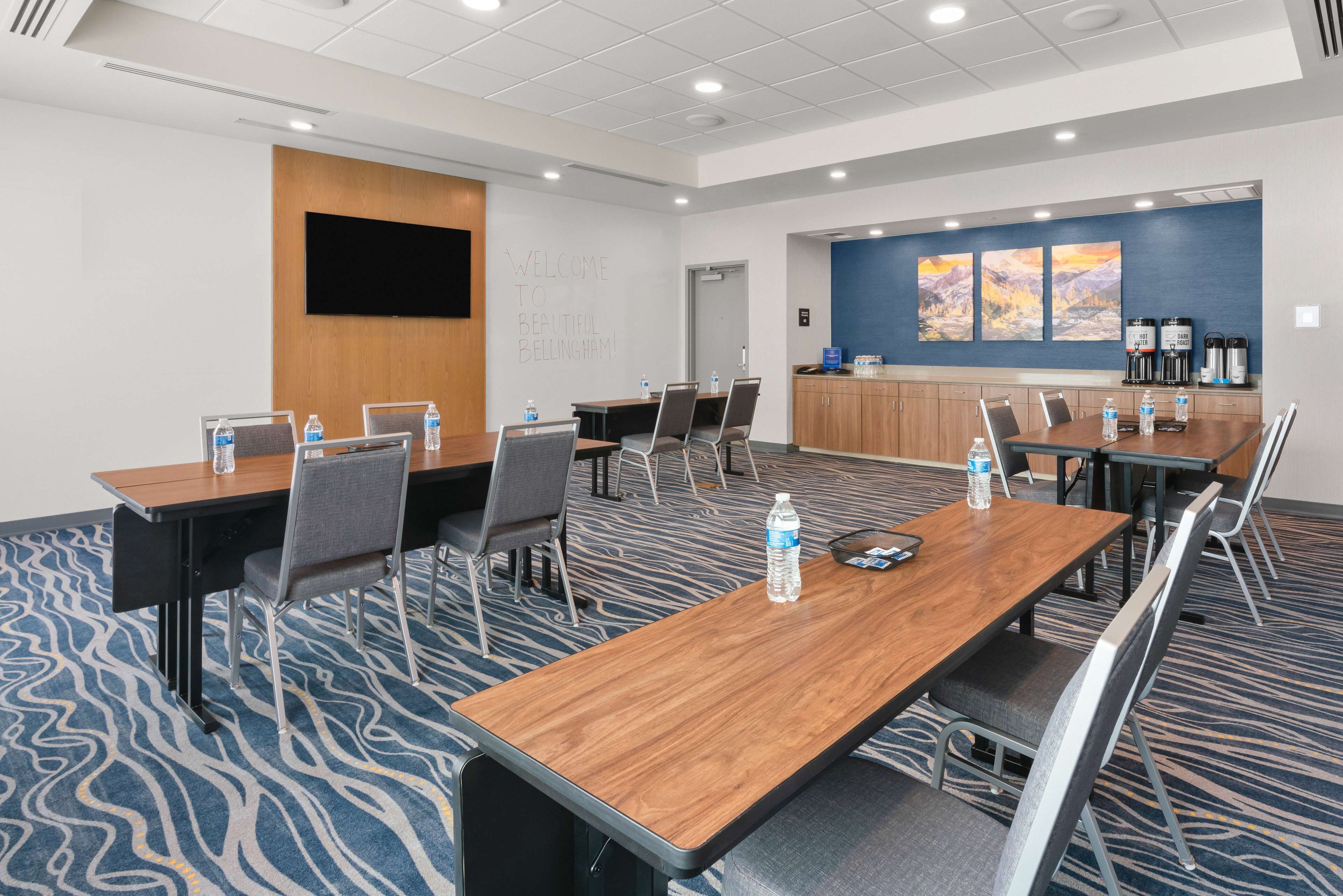 A conference room with a long table, chairs, a whiteboard, and a wall-mounted TV.