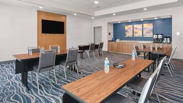 A conference room with a long table, chairs, a whiteboard, and a wall-mounted TV.