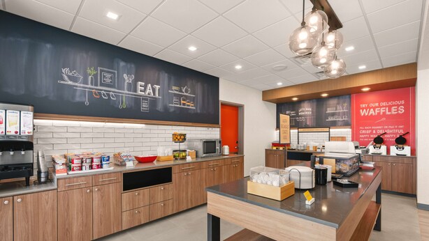 A modern kitchen area with a chalkboard menu, a coffee station, and a waffle station.