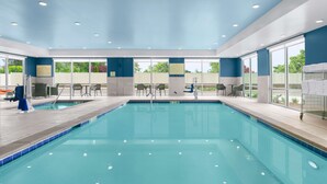 An indoor swimming pool with clear water, surrounded by blue walls and large windows.