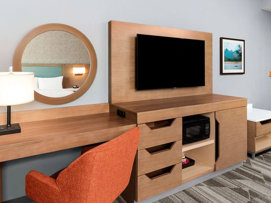 Habitación de hotel con un escritorio de madera, un televisor de pantalla plana, un espejo y un cuadro en la pared.