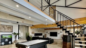 Un grand espace de vie comprenant un billard, un escalier et un coin cuisine.