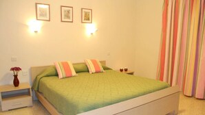 Une chambre à coucher comprenant un lit, deux tables de chevet, une commode, un vase avec des fleurs et deux lampes fixées au mur.