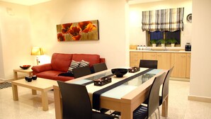 Un salon moderne avec un canapé rouge, une table à manger avec des chaises, un tableau accroché au mur et un coin cuisine agrémenté d’un lambrequin à rayures.