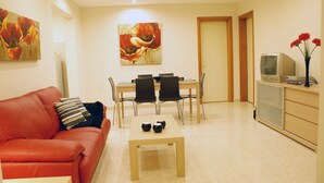 Un espace de vie compact comprenant un canapé rouge, une table à manger avec quatre chaises, une petite table basse et un téléviseur posé sur un meuble.