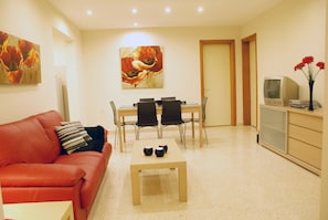 A compact living space with a red sofa, a dining table with four chairs, a small coffee table, and a TV on a cabinet. - Villa Margherita Unit 1, with a large Pool, patio, and spacious outside spaces. (Mellieha)