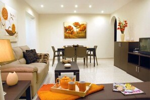 Uma sala de estar moderna com um sofá, mesa de centro e área de jantar. Há uma televisão num móvel e um quadro na parede.