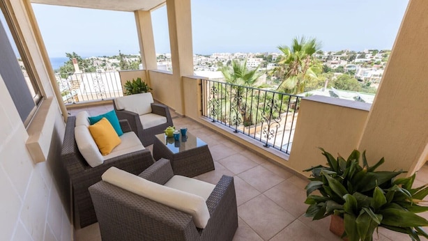 Een balkon met rieten meubels, een glazen bijzettafeltje en potplanten.