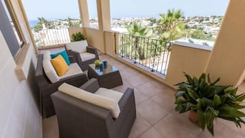 A balcony with wicker furniture, a glass coffee table, and potted plants.