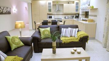 A living room with a sofa, coffee table, and a dining area with chairs and a kitchen in the background.