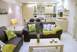 Un salon avec un canapé, une table basse et un coin repas comprenant des chaises, et une cuisine en arrière-plan.