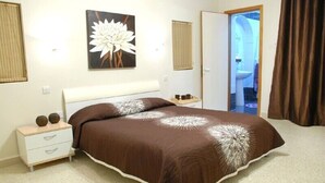 Een slaapkamer met een groot bed, een nachtkastje met twee decoratieve objecten, een aan de muur hangend schilderij en een deur naar een badkamer.