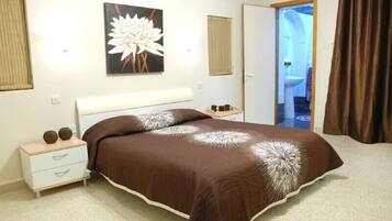 A bedroom with a large bed, a bedside table with two decorative items, a wall-mounted painting, and a door leading to a bathroom.