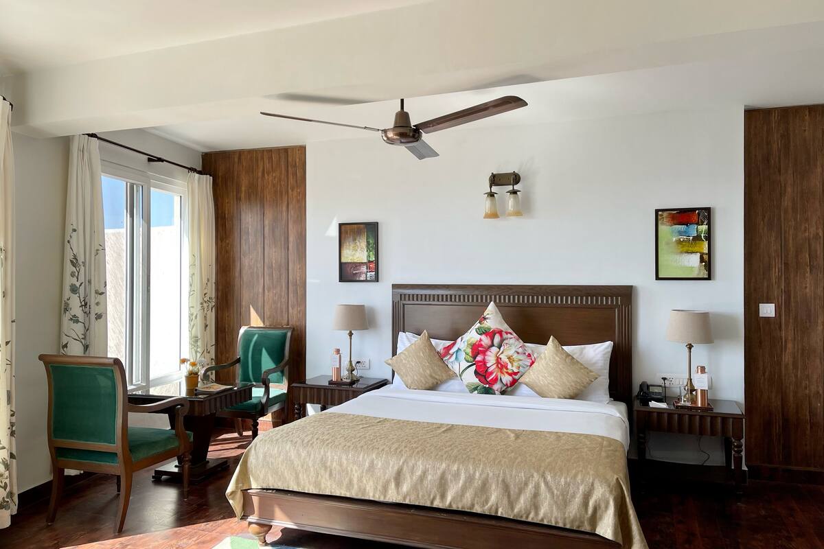 A hotel room with a large bed, a desk, a chair, a ceiling fan, and artwork on the walls.