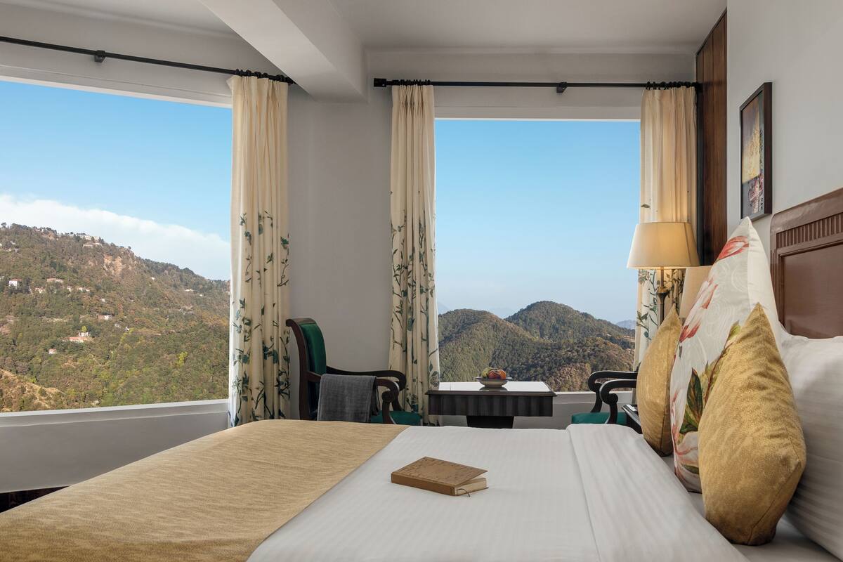 A hotel room with a bed, a table, and a chair. The room has a view of a mountainous landscape.