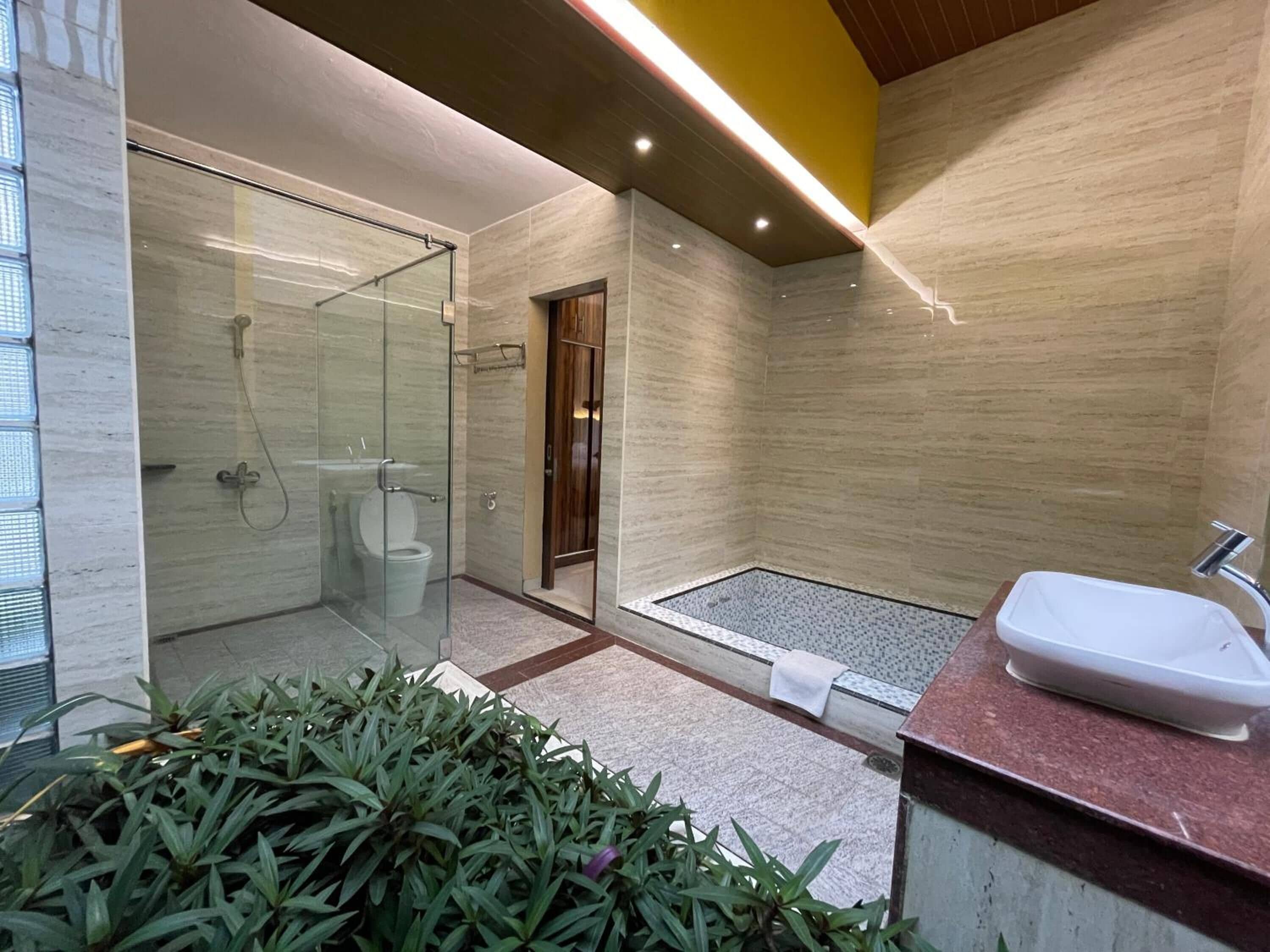Un baño moderno con ducha de vidrio, inodoro separado y lavamanos con encimera de mármol.