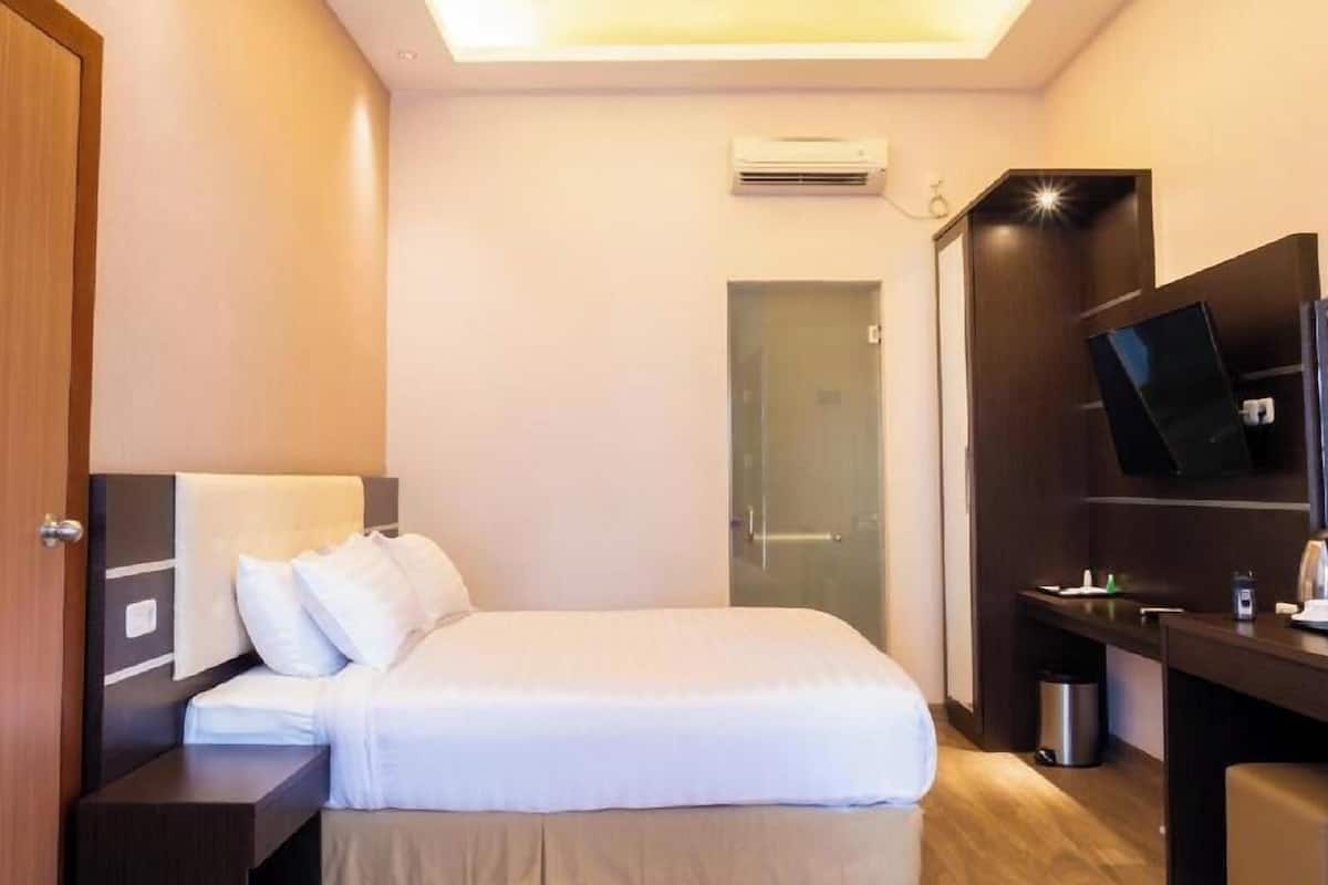Une chambre d’hôtel comprenant un lit, une table de chevet, une télévision et un petit bureau avec une chaise.