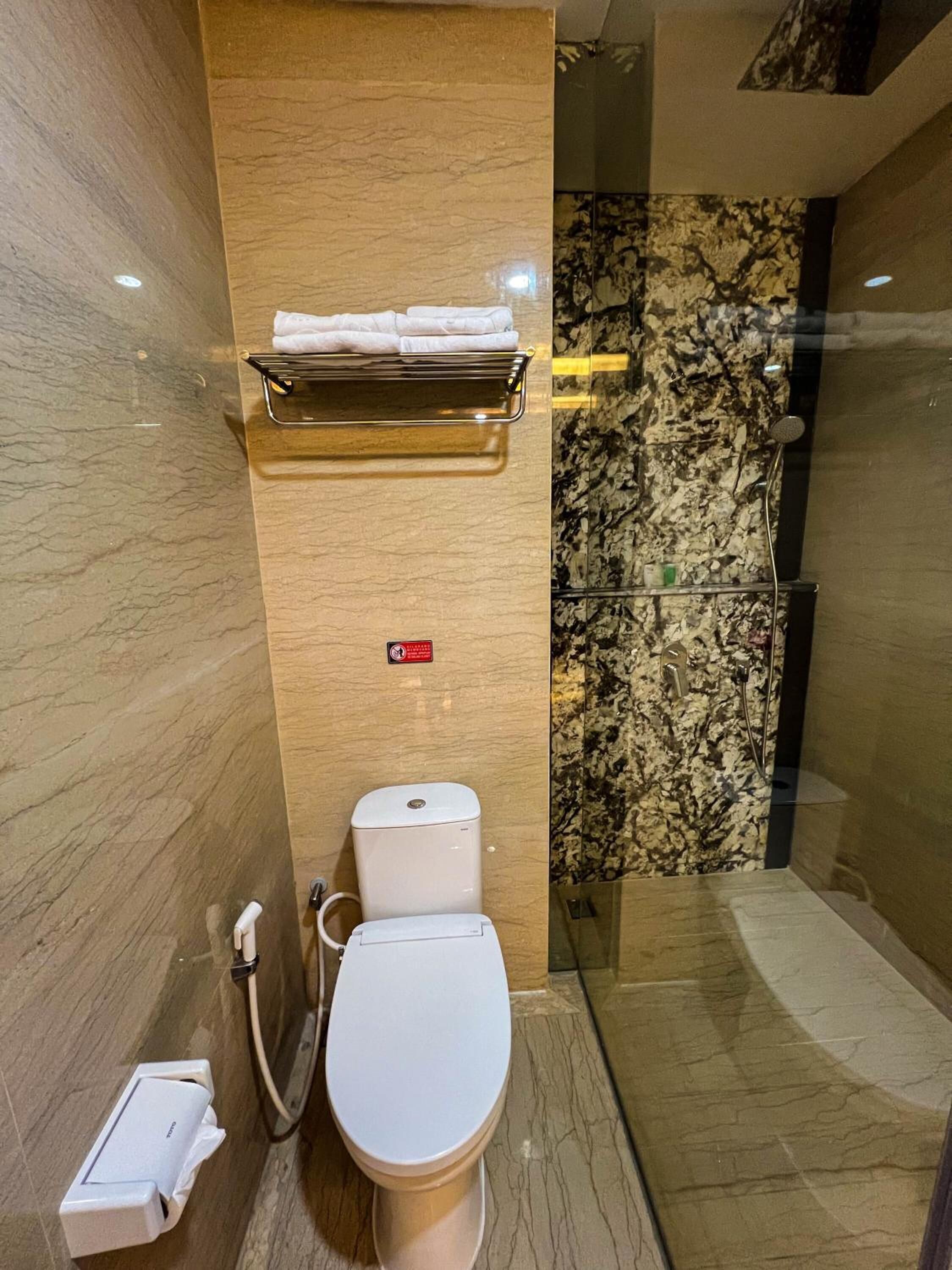 A modern bathroom with a marble wall, a toilet, a shower, and a towel rack.