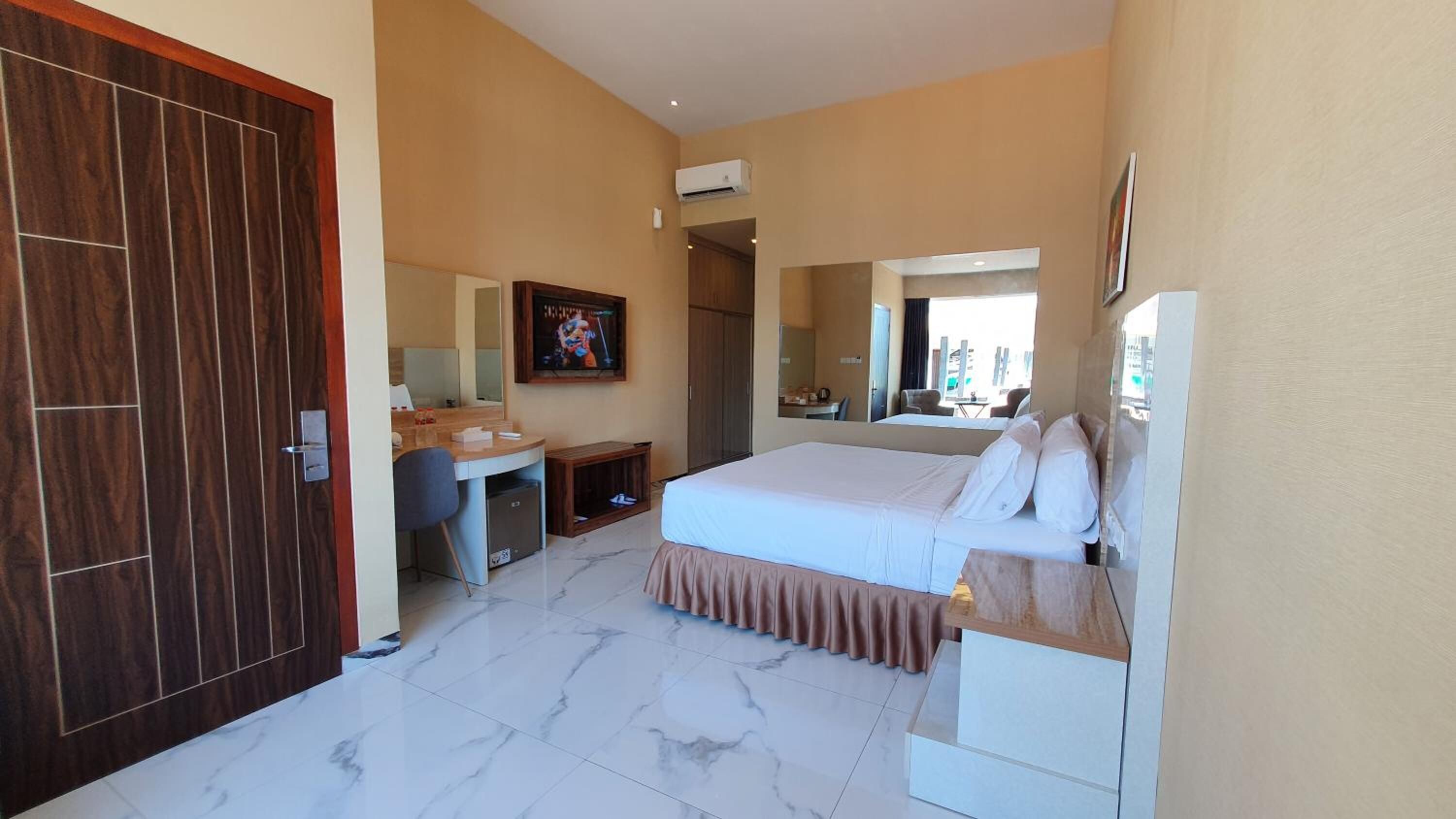 A hotel room with a bed, a desk, a chair, a mirror, and an air conditioning unit.