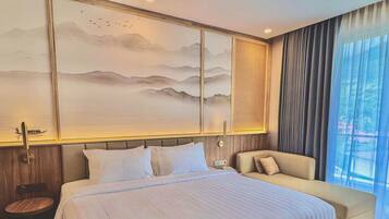 A hotel room with a large bed, a sofa, a small round table, and a large window with curtains.