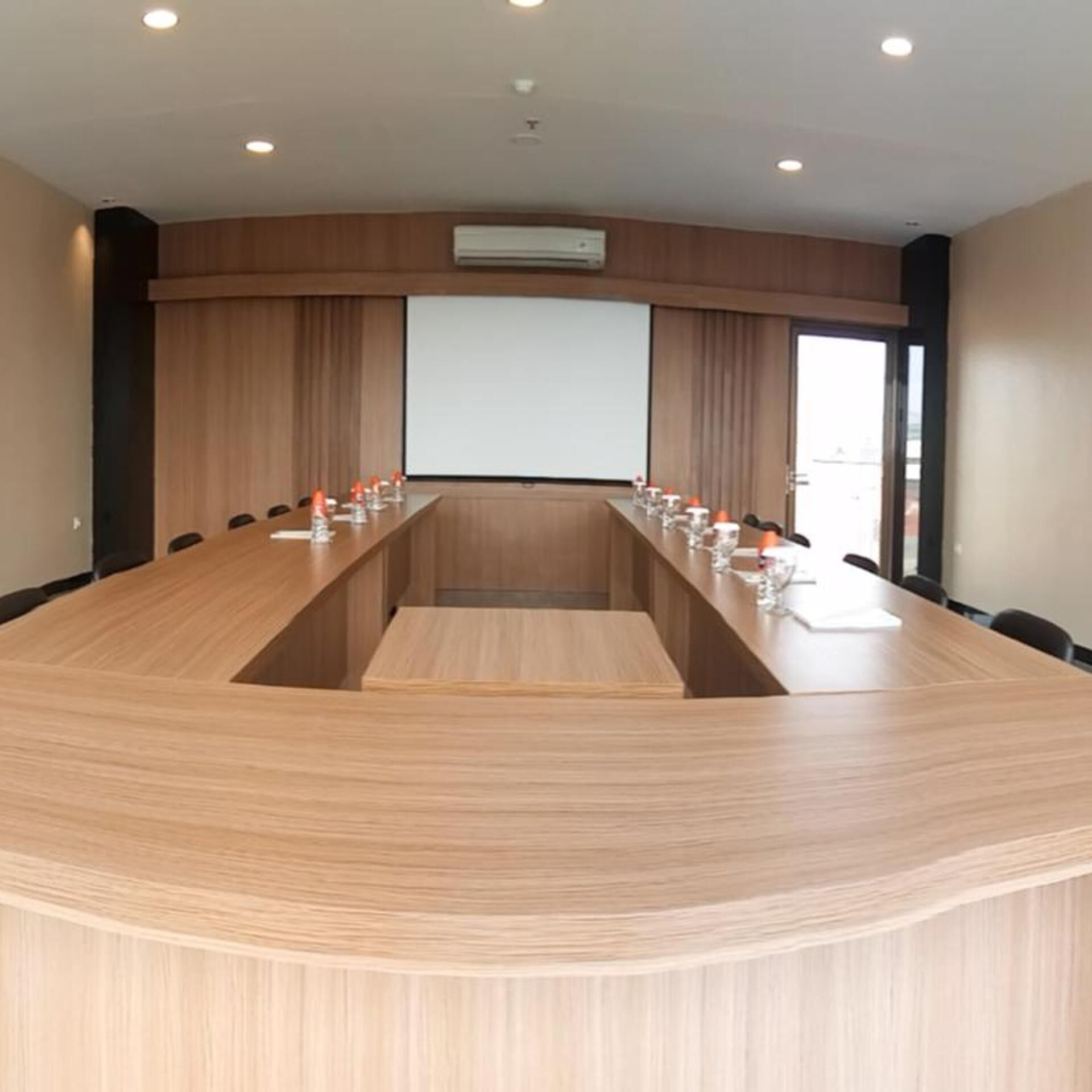 A conference room with a long table, chairs, a projector screen, and an air conditioning unit.