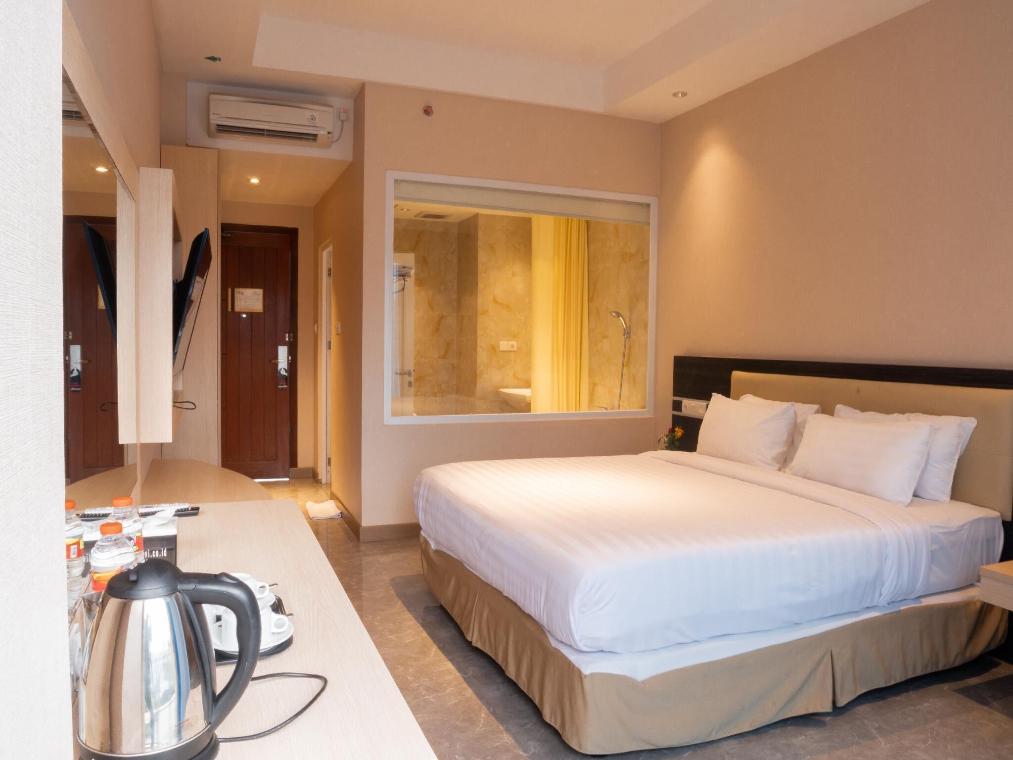 A hotel room with a bed, a desk with a kettle, and a large mirror.