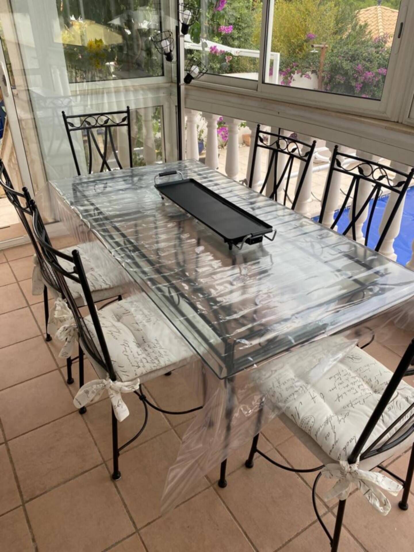 A glass-enclosed patio table with a tray, surrounded by chairs with white cushions tied with ribbons.