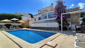 A swimming pool with lounge chairs and umbrellas, surrounded by a stone wall and a building with large windows and a balcony. - Superb summer house with swimming pool, parking, wifi and air conditioning  (L'Escala)