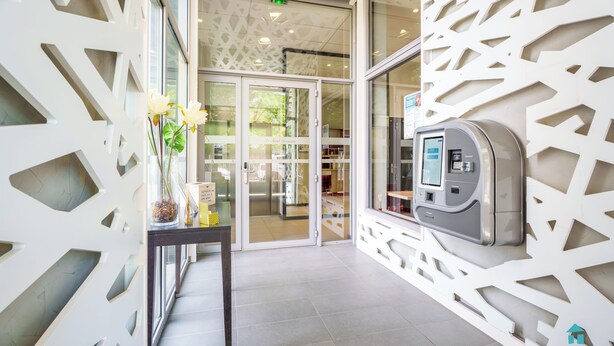 A modern entrance with a decorative white wall, a glass door, and a payment kiosk. - Tempologis Le Saint Germain Grenoble (Grenoble)