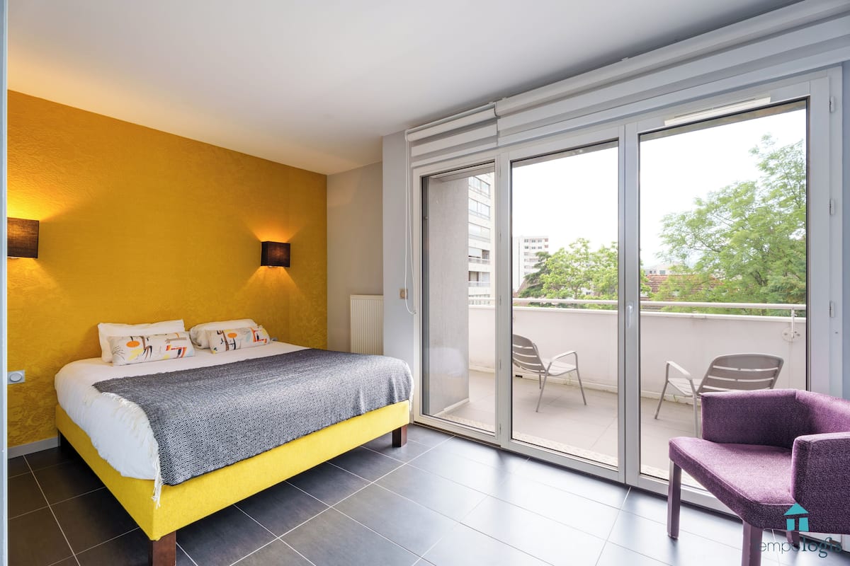 A bedroom with a bed, a chair, and a balcony with a view.