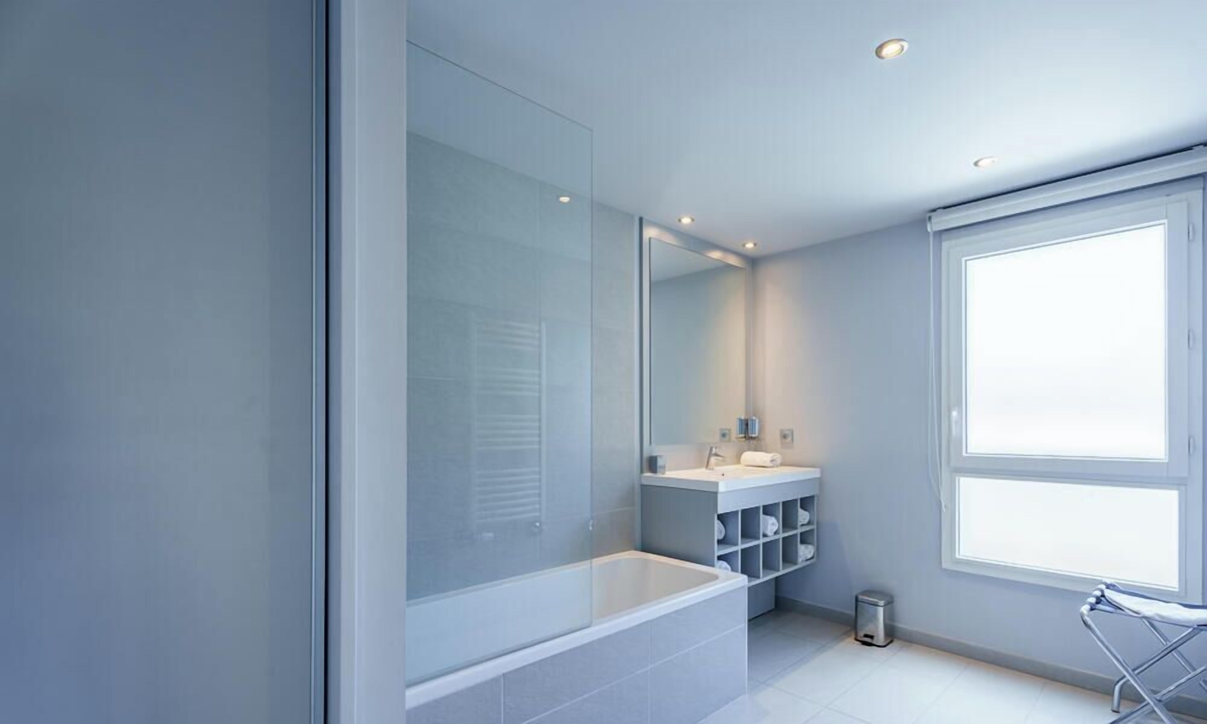 Ein modernes Badezimmer mit einer Badewanne, einem großen Spiegel, einem Fenster und einem Waschbecken mit Ablageflächen.
