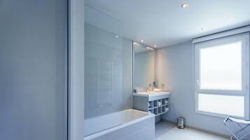 Ein modernes Badezimmer mit einer Badewanne, einem großen Spiegel, einem Fenster und einem Waschbecken mit Ablageflächen.