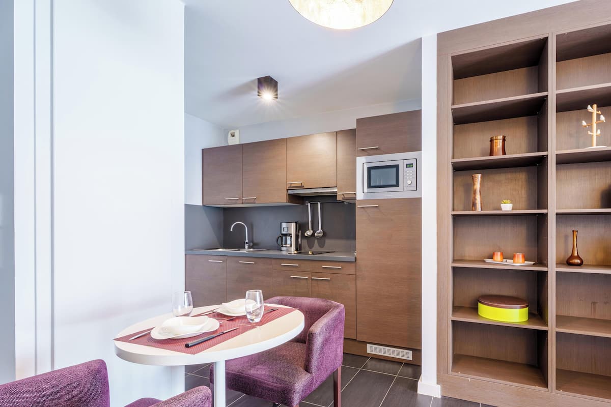 A modern kitchen with a microwave, sink, and coffee maker. There is a dining area with a table and purple chairs.