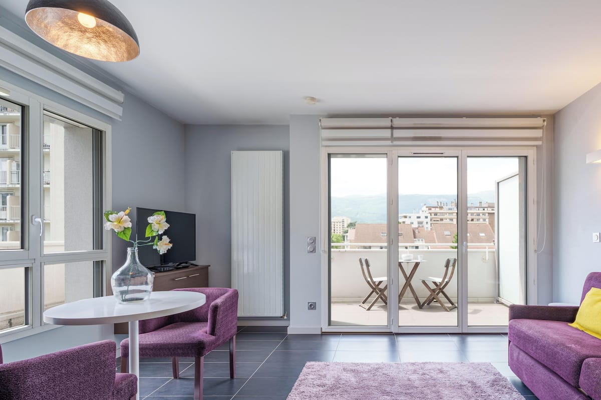 Un salon moderne avec un canapé violet, une petite table ronde et un téléviseur.