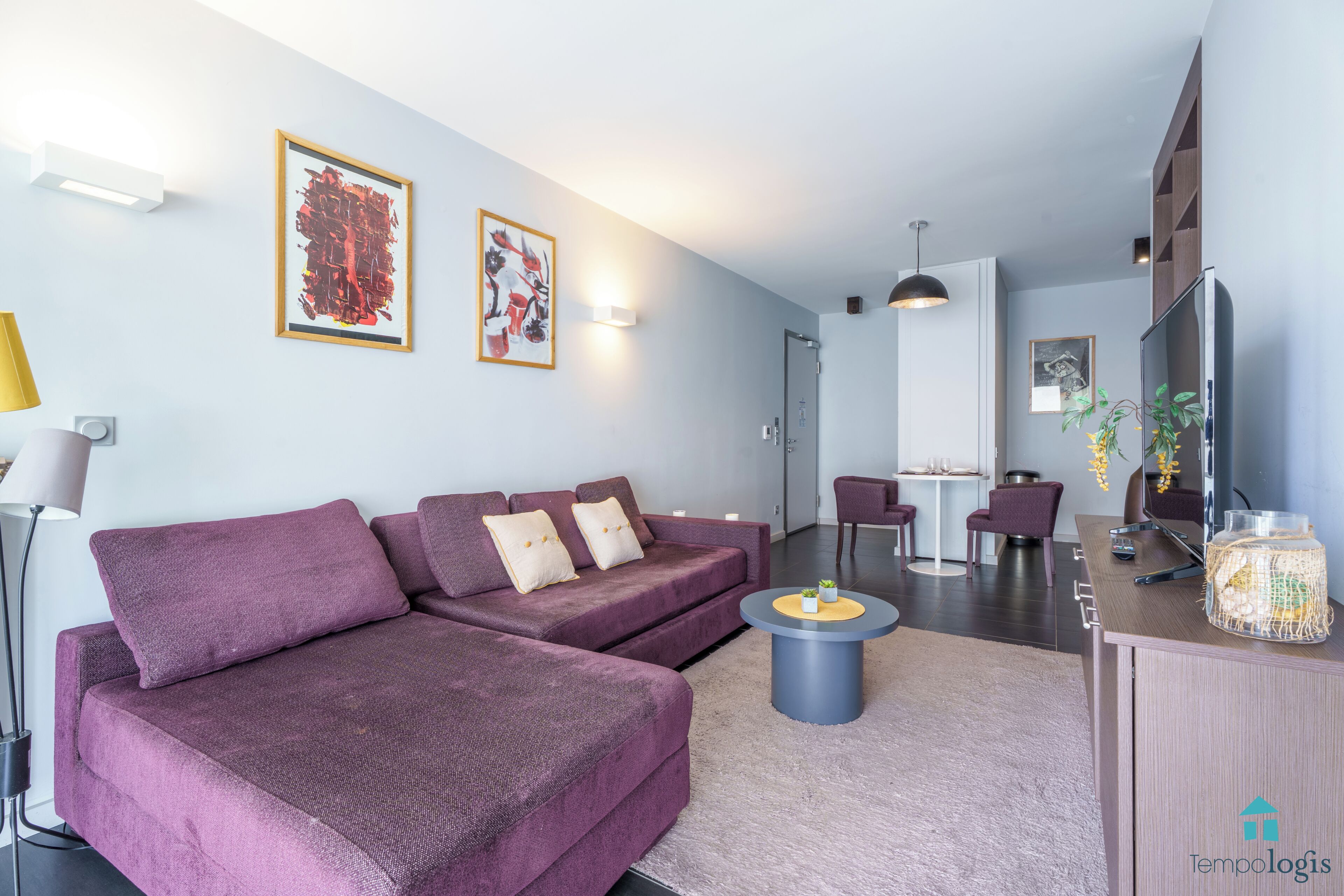 Un salon moderne avec un canapé d’angle, une table basse ronde et un téléviseur à écran plat.