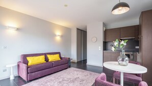 A modern living room with a purple sofa, a white table, and a kitchen area with dark cabinets. - Tempologis Le Saint Germain Grenoble (Grenoble)
