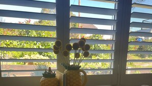 A table with a pineapple-shaped vase and a decorative pineapple, a large green leaf placemat, and a window with horizontal blinds. - Highlands Escape  Moss Vale (Moss Vale)