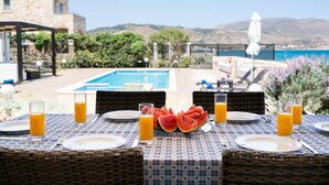 A dining table with plates, glasses, and watermelon slices, overlooking a pool and mountains. - Beachfront villa w/private pool, ping pong and BBQ (Chania)