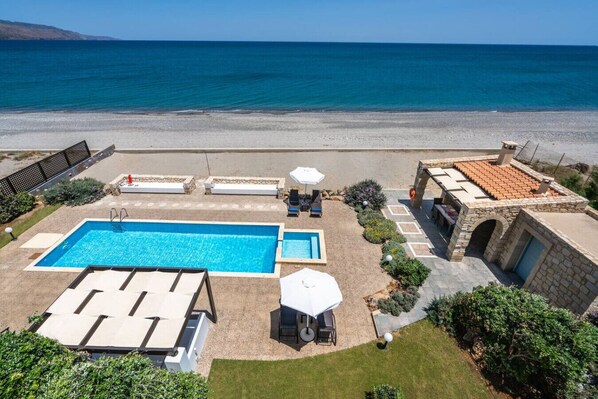 A swimming pool with lounge chairs and umbrellas, a stone patio, and a view of the sea.