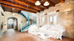A spacious living area with a white couch, a coffee table, a blue staircase, and stone walls. - Beachfront villa w/private pool, ping pong and BBQ (Chania)