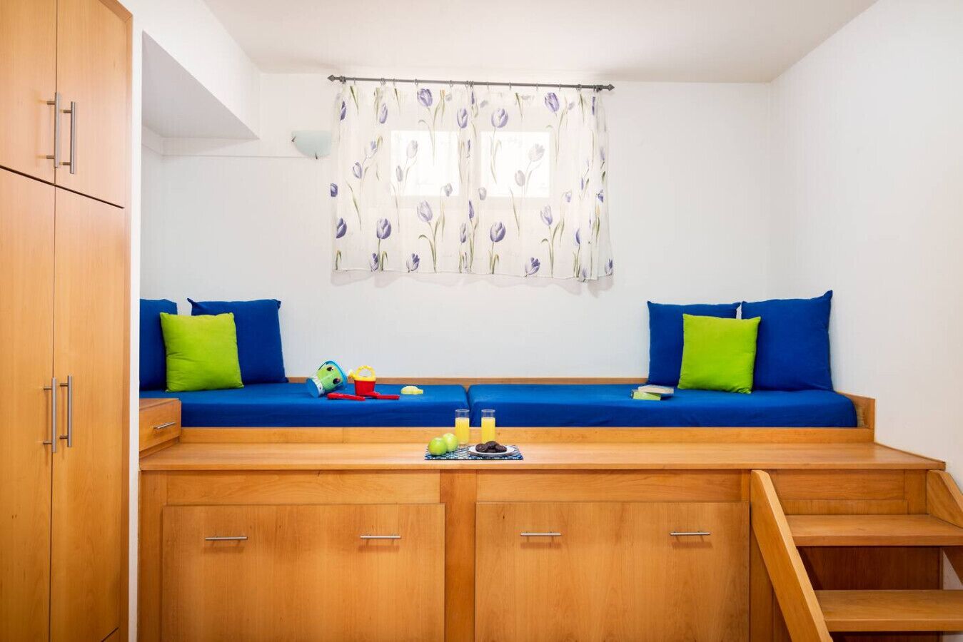 A room with a blue sofa, green cushions, wooden cabinets, and a window with a floral curtain.