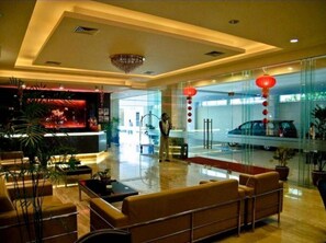 A hotel lobby with a reception desk, seating area, and a glass wall with a car visible through it.