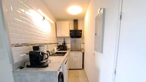 Una cocina compacta con salpicadero de azulejos blancos, lavadora integrada y microondas.