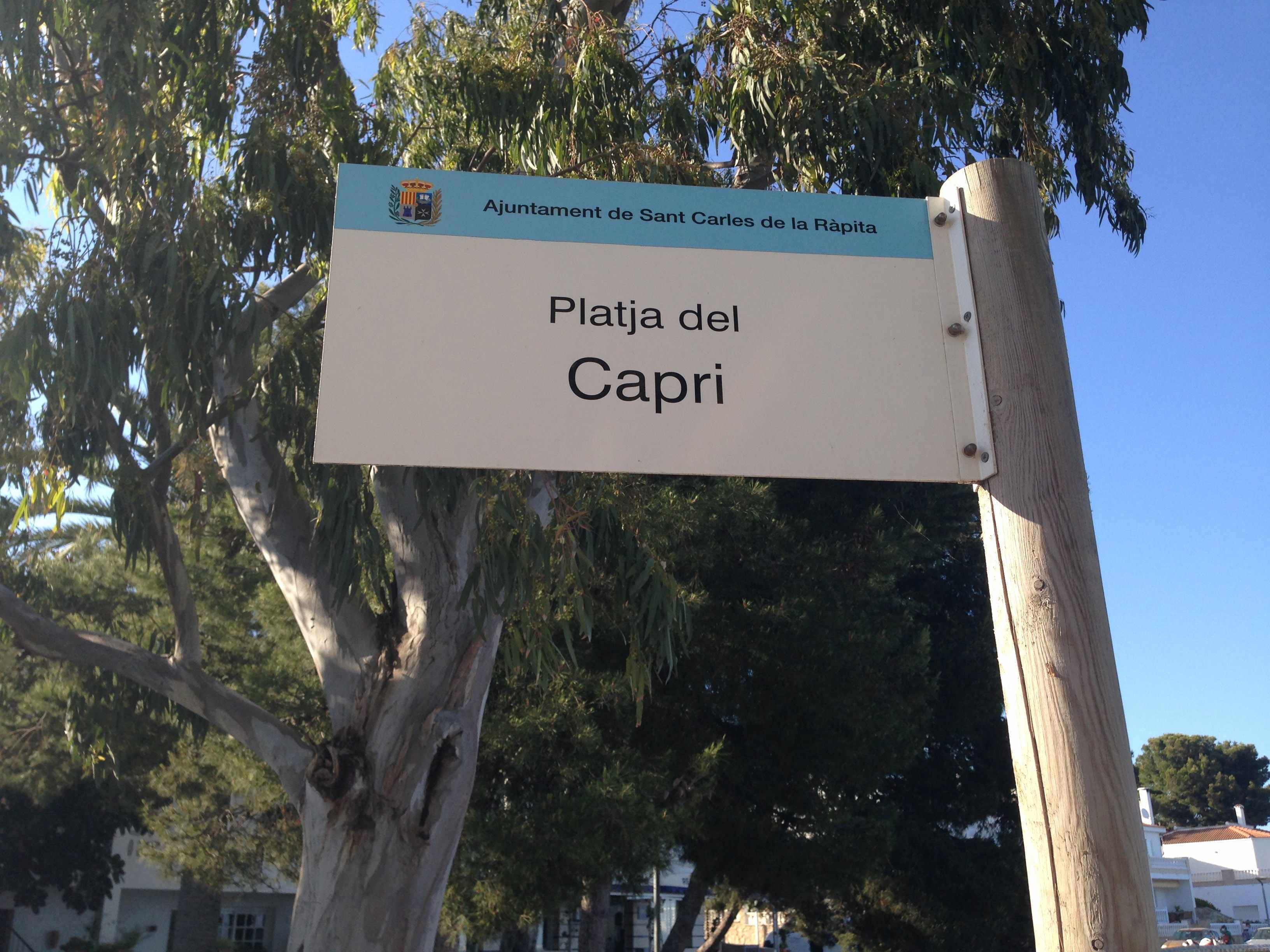Une enseigne indiquant « Playa del Capri », avec un blason et un texte précisant qu’elle fait partie de la « municipalité de Sant Carles de la Ràpita ».