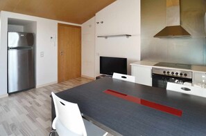 A modern kitchen with a stainless steel refrigerator, a flat-screen TV, and a gas stove.