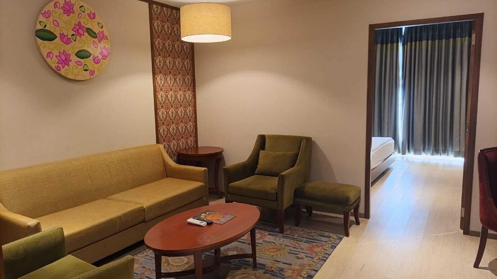 Una sala de estar con sofá, sillón y mesa de centro, una pared con diseño, y vista a través de una ventana con cortinas.