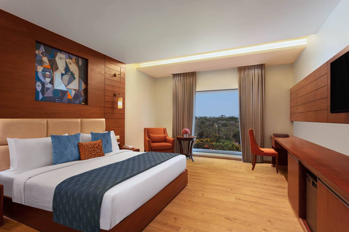 A modern hotel room with a large bed, a desk, a chair, and a TV.