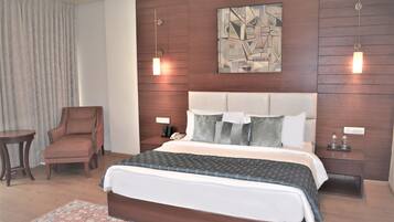 Een moderne hotelkamer met een groot bed, een fauteuil, een nachtkastje en een kunstwerk aan de muur.